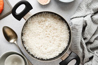Overhead view of pot of white rice on a counter next to a serving spoon and a gray towel