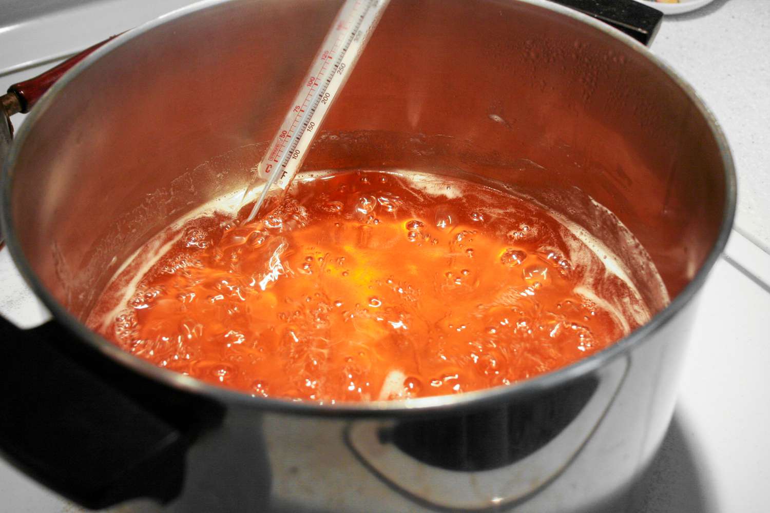 A pot of boiling quince jelly with a thermometer