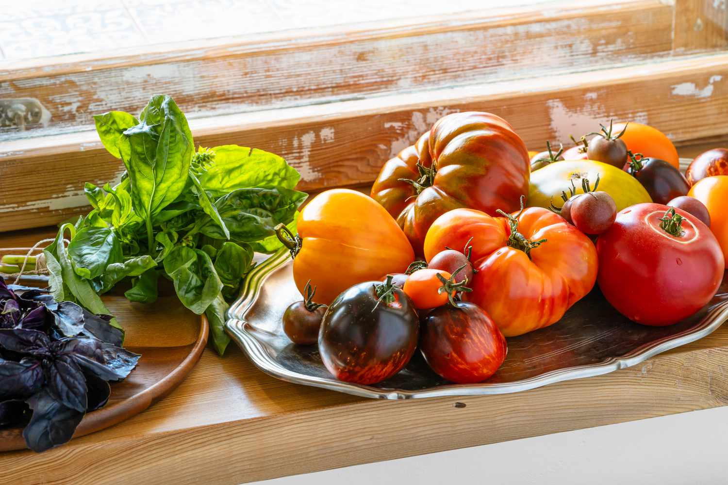fresh heirloom tomatoes on a platter next to a plate with fresh basil (green and purple)
