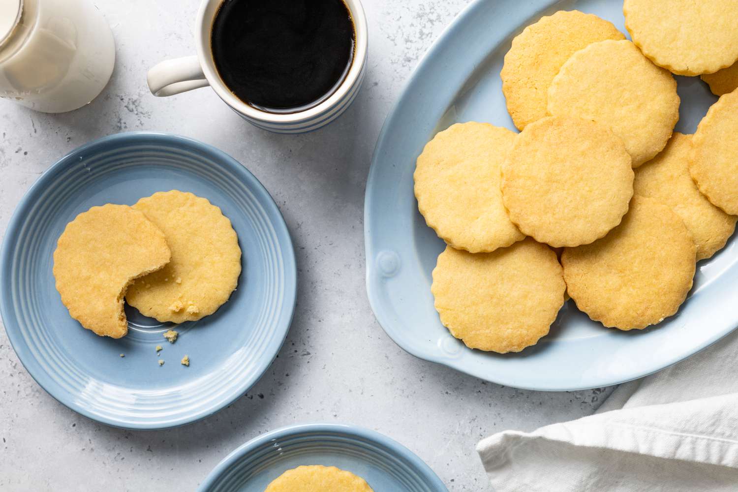 Classic Shortbread Cookies on a Plate with One Bitten from Next to a Plate with More Cookies and a Cup of Coffee
