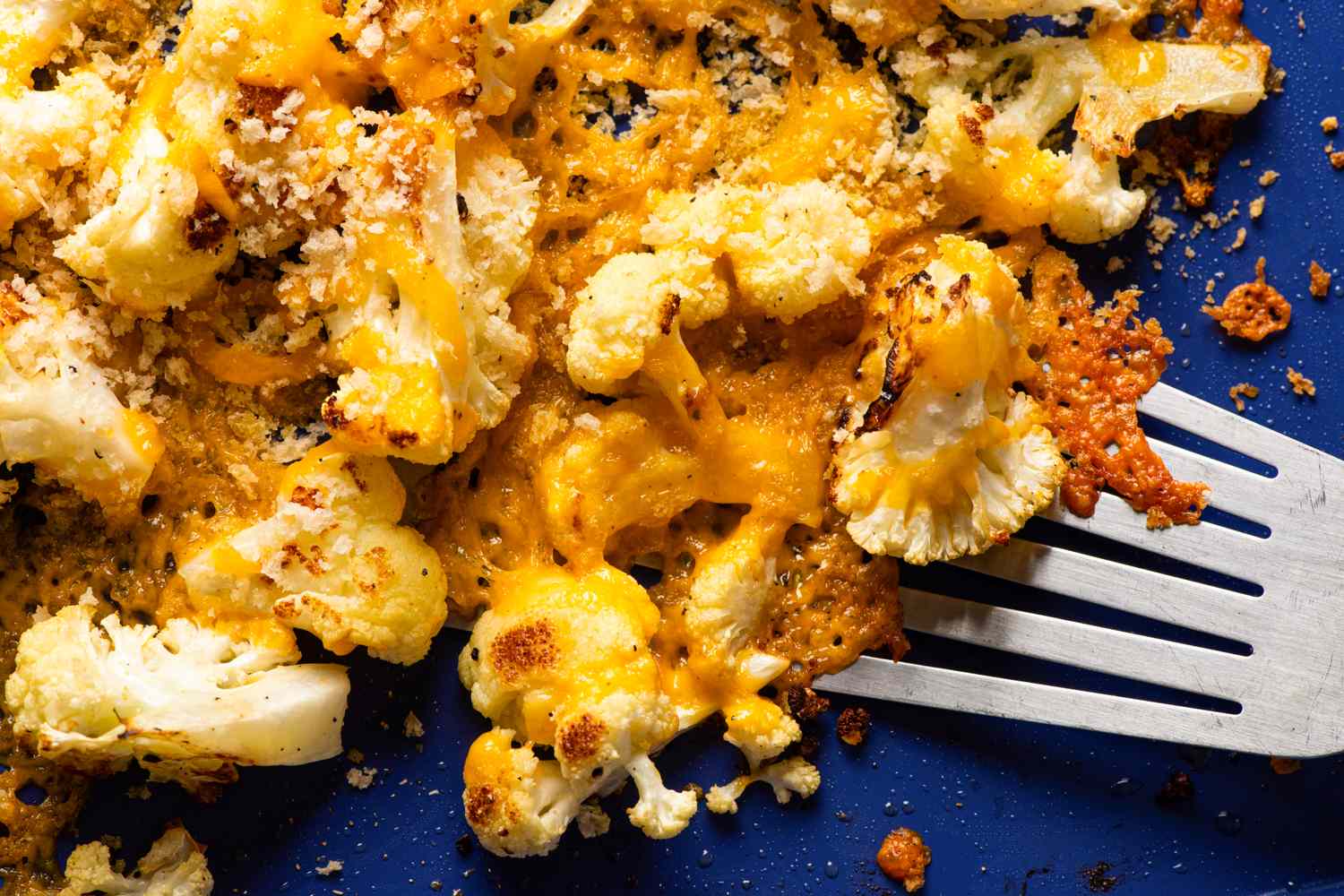 Roasted cauliflower topped with melted cheese and breadcrumbs with a fork on the side on a blue plate