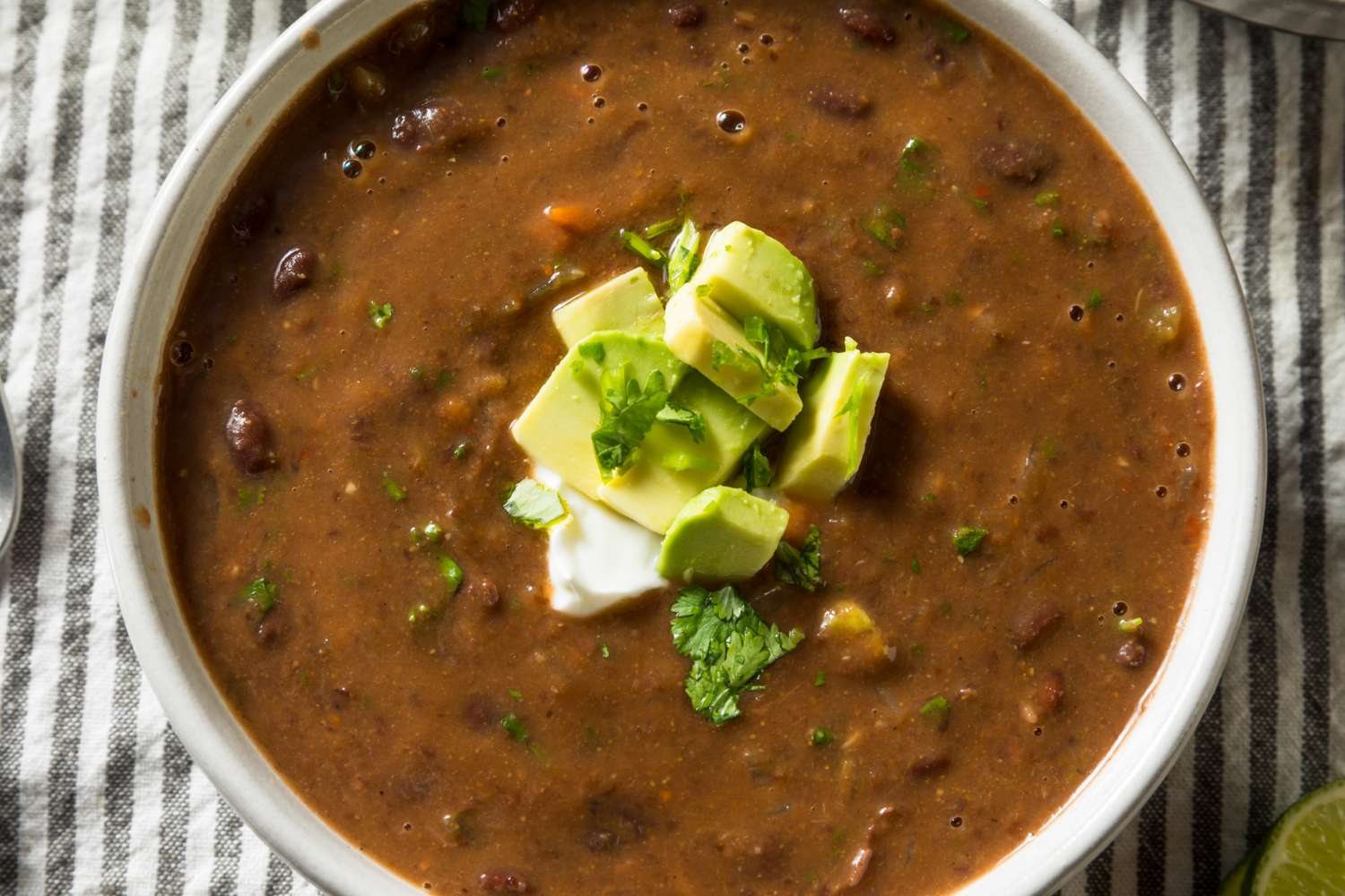 A bowl of bean soup garnished with chopped avocado cilantro and a dollop of sour cream