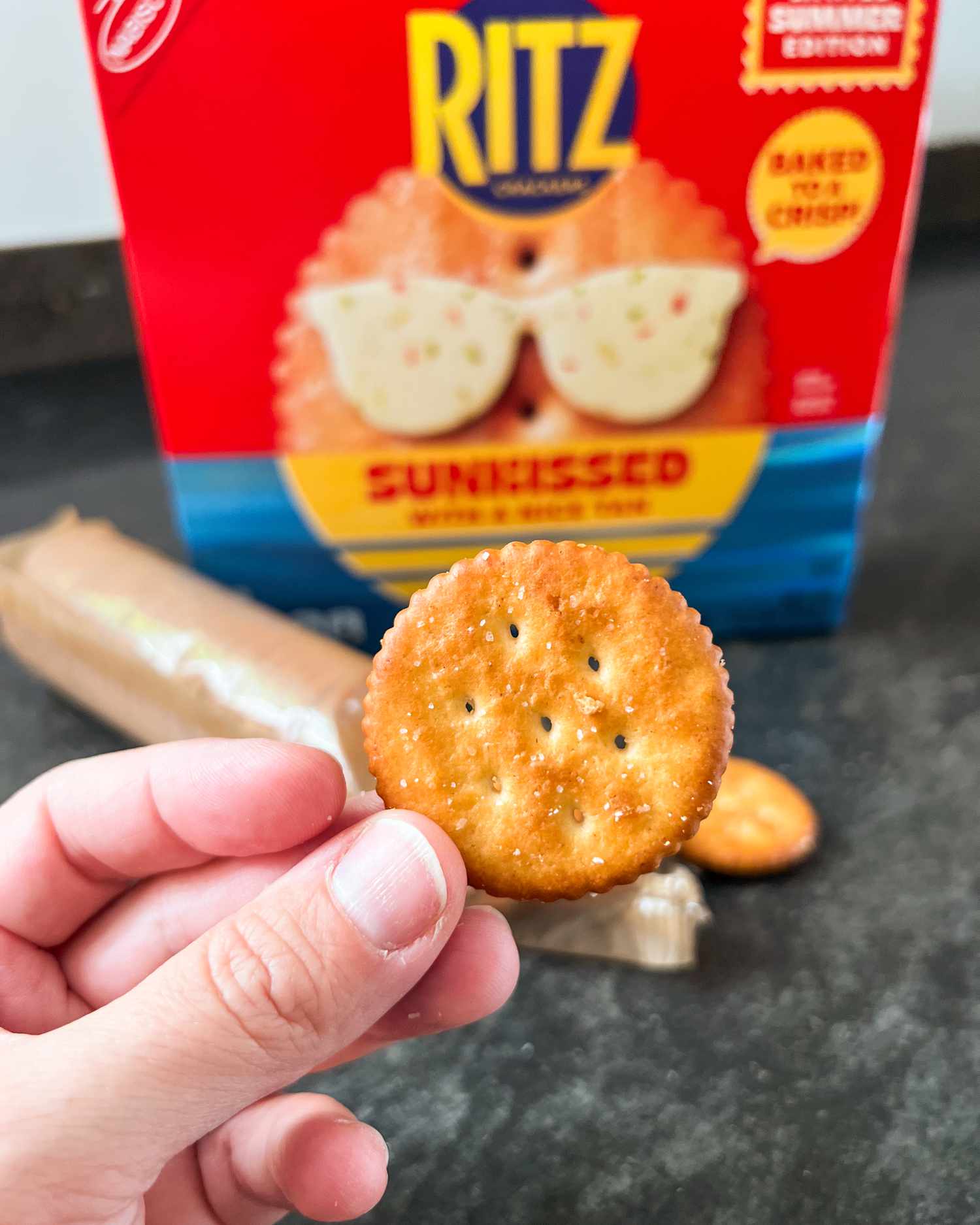 Sunkissed Ritz box in the background with a hand holding a cracker in the foreground
