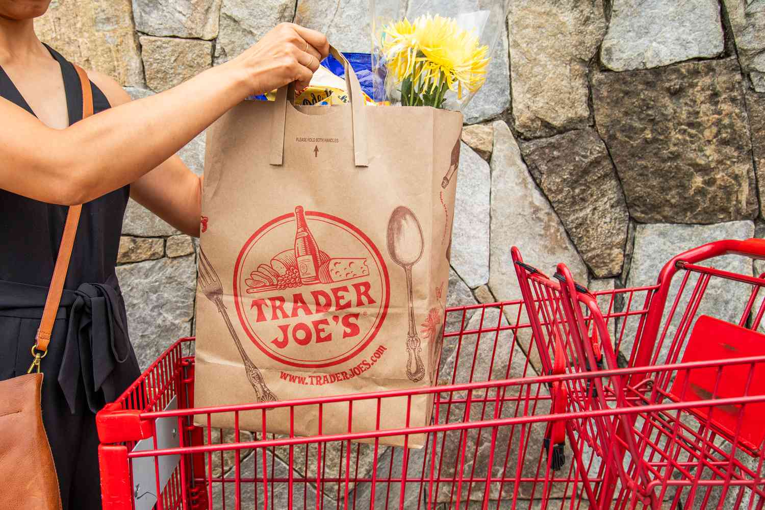 Someone lifting a trader joe's bag from a shopping cart 