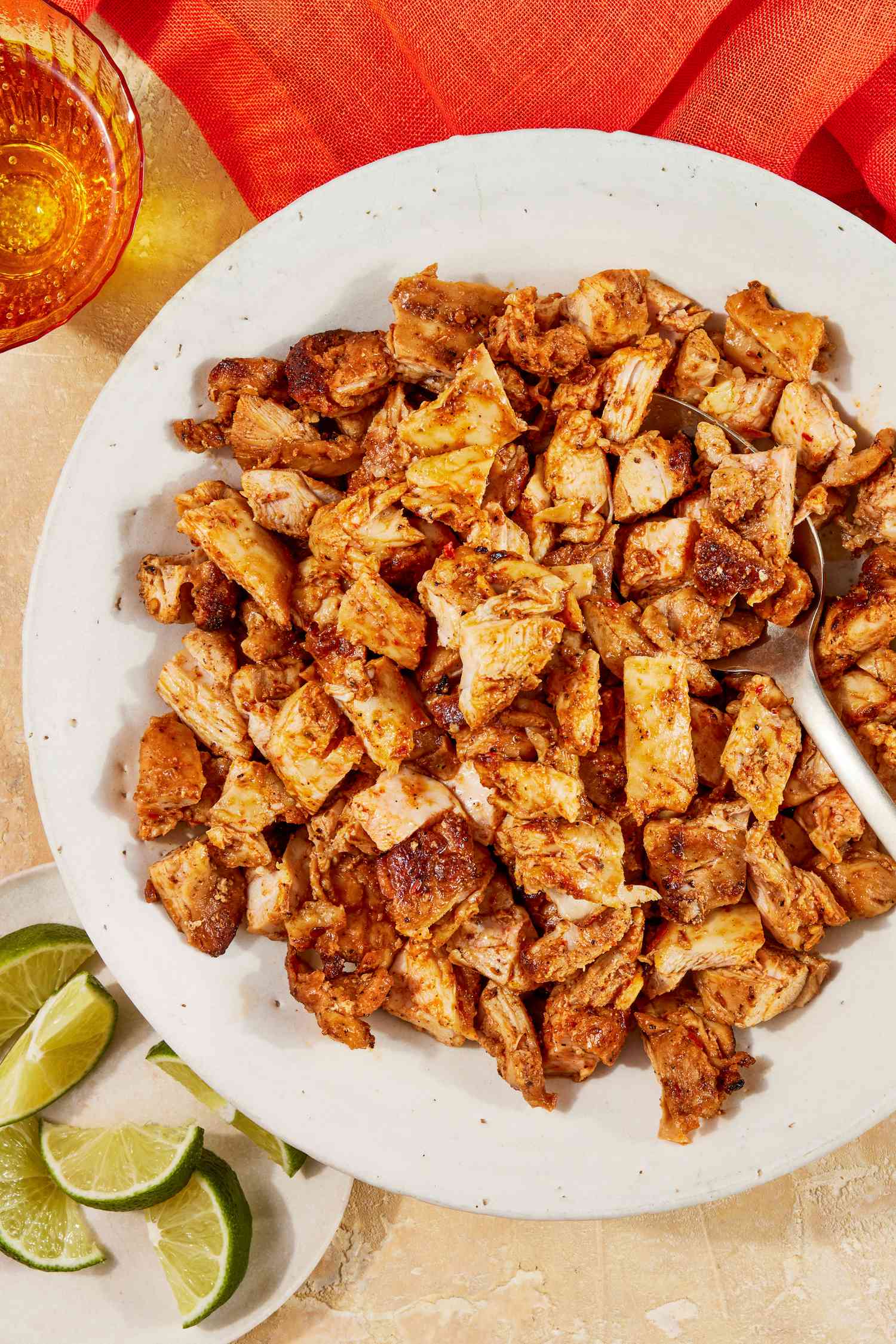 Bowl of copycat Chipotle chicken with a spoon at a table setting with a small plate of lime quarters, glasses of water, and a scarlet table napkin