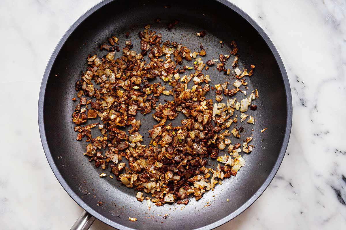 Caramalized chopped onions in a saute pan on a marble background.