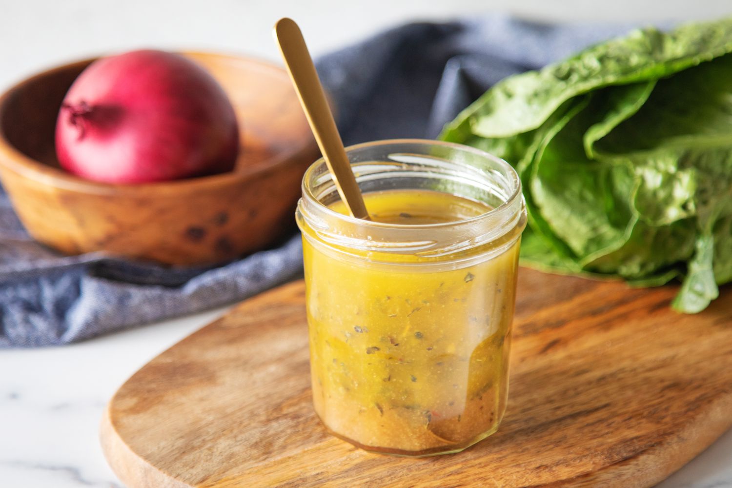 An open jar if Italian dressing on a cutting board with a spoon in it