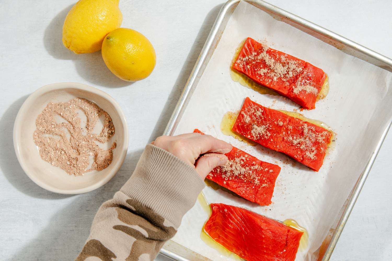 Salmon fillets on a baking sheet being sprinkled with spices