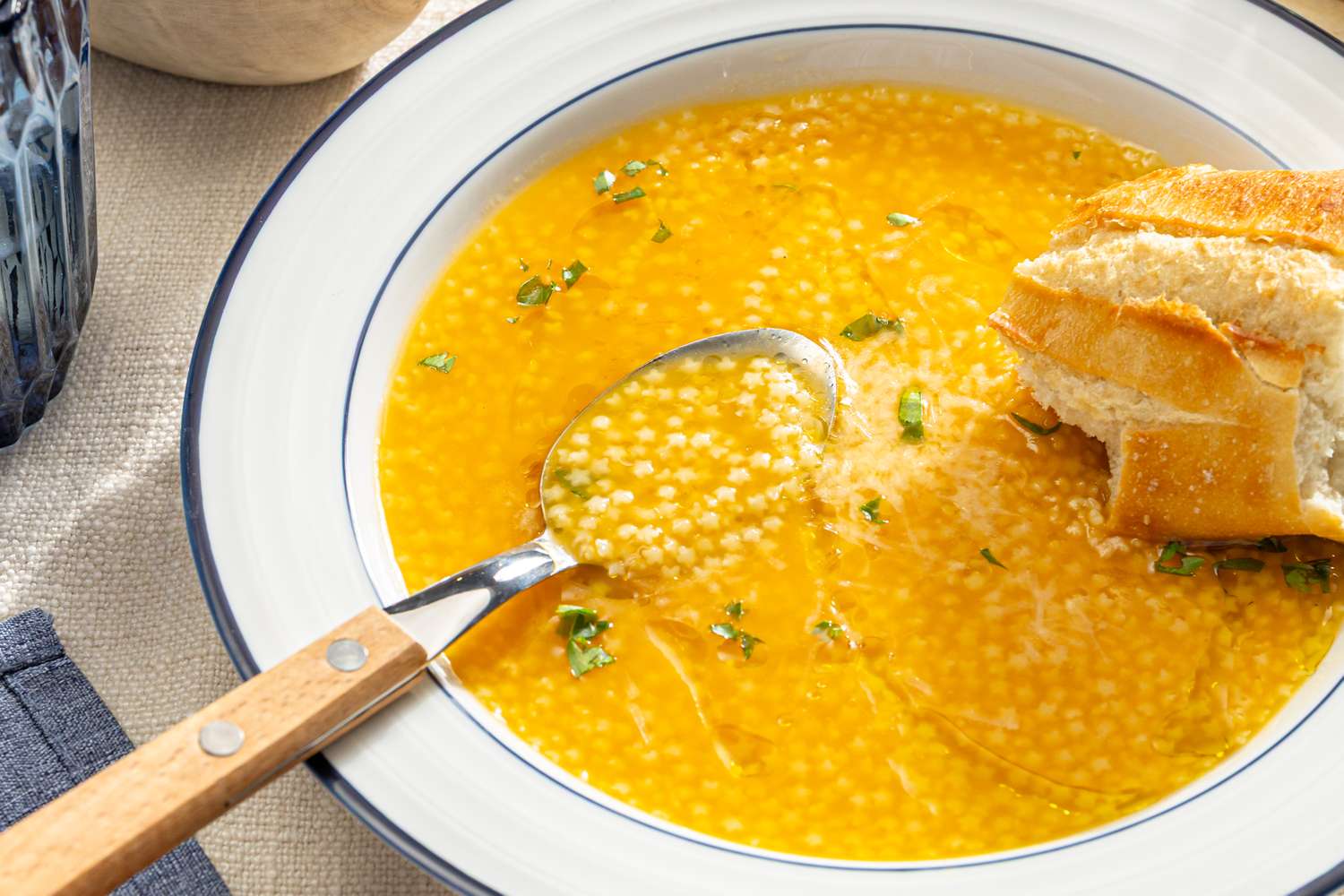 A bowl of pastina soup with a spoon and a piece of bread