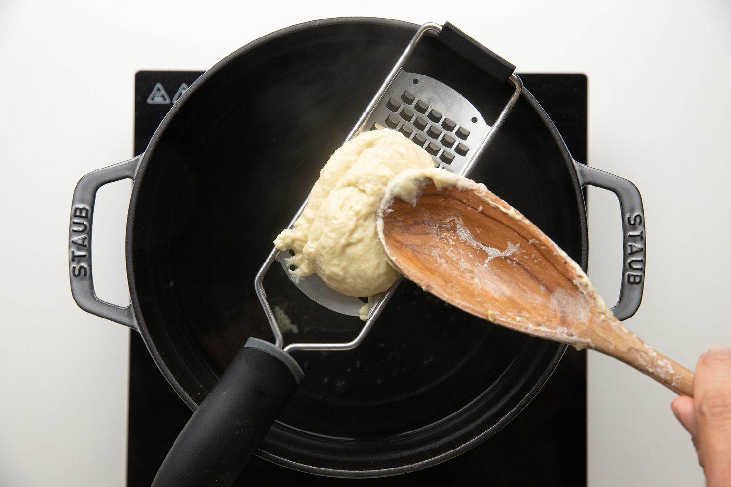 Spoonful of Spaetzle Dough Placed on the Smooth Side of a Cheese Grater Over a Dutch Oven Filled with Boiling Water