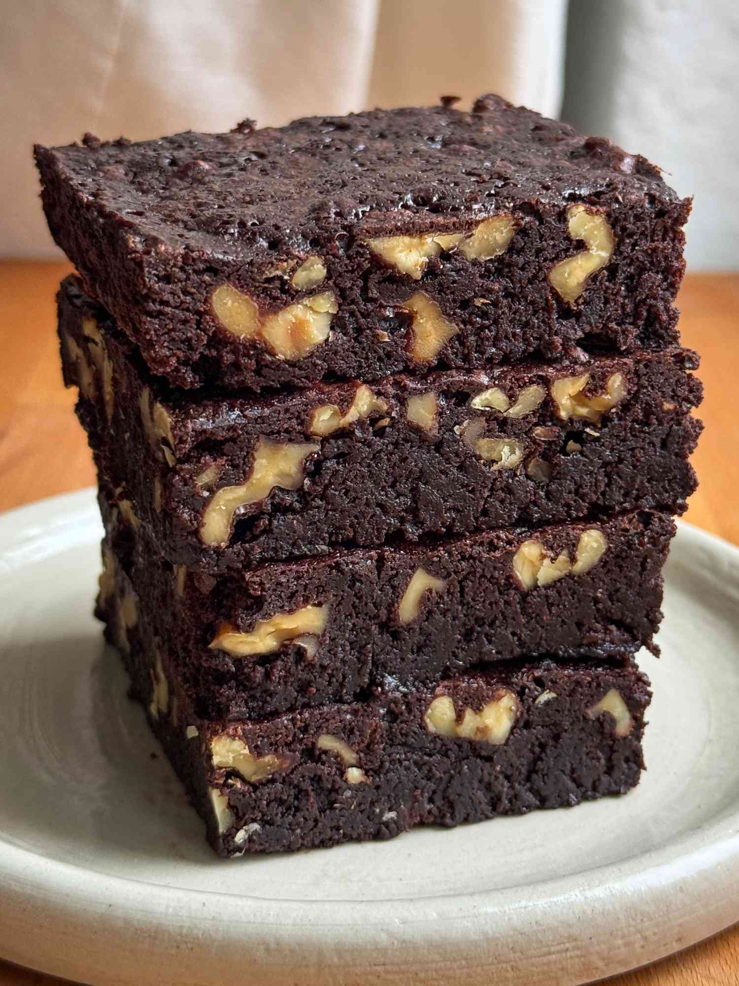 A stack of dark chocolate brownies studded with walnuts on a small ceramic plate
