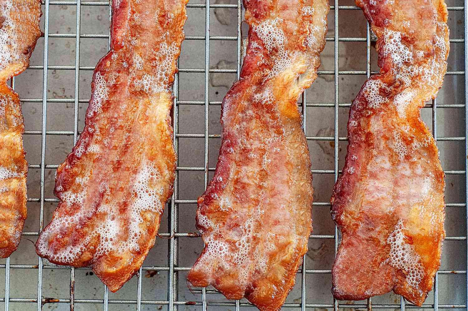 Four slices of oven baked bacon on a cooling rack.