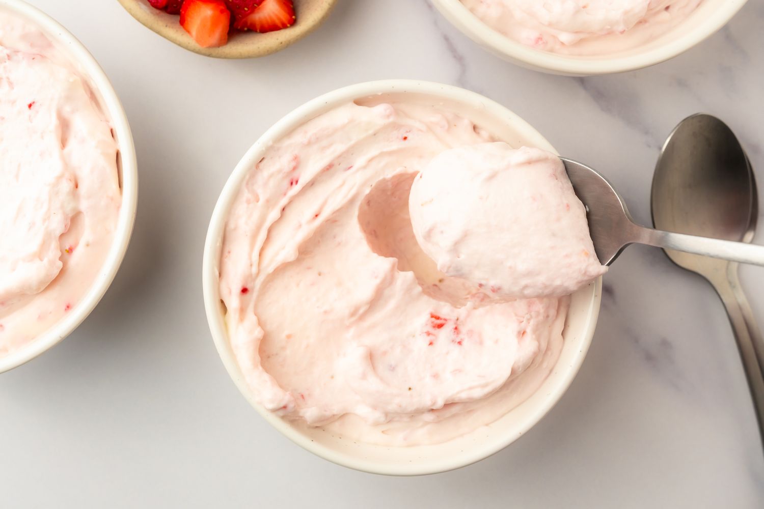 A bowl of strawberry mousse with a spoon scooping some out additional dishes in the background