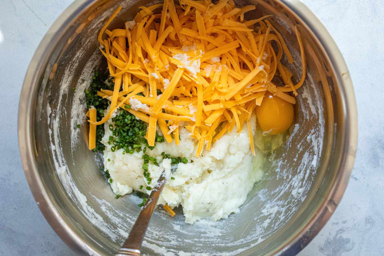 Cheese, egg, and chives added to a mashed potatoes to make cheesy leftover mashed potato pancakes.