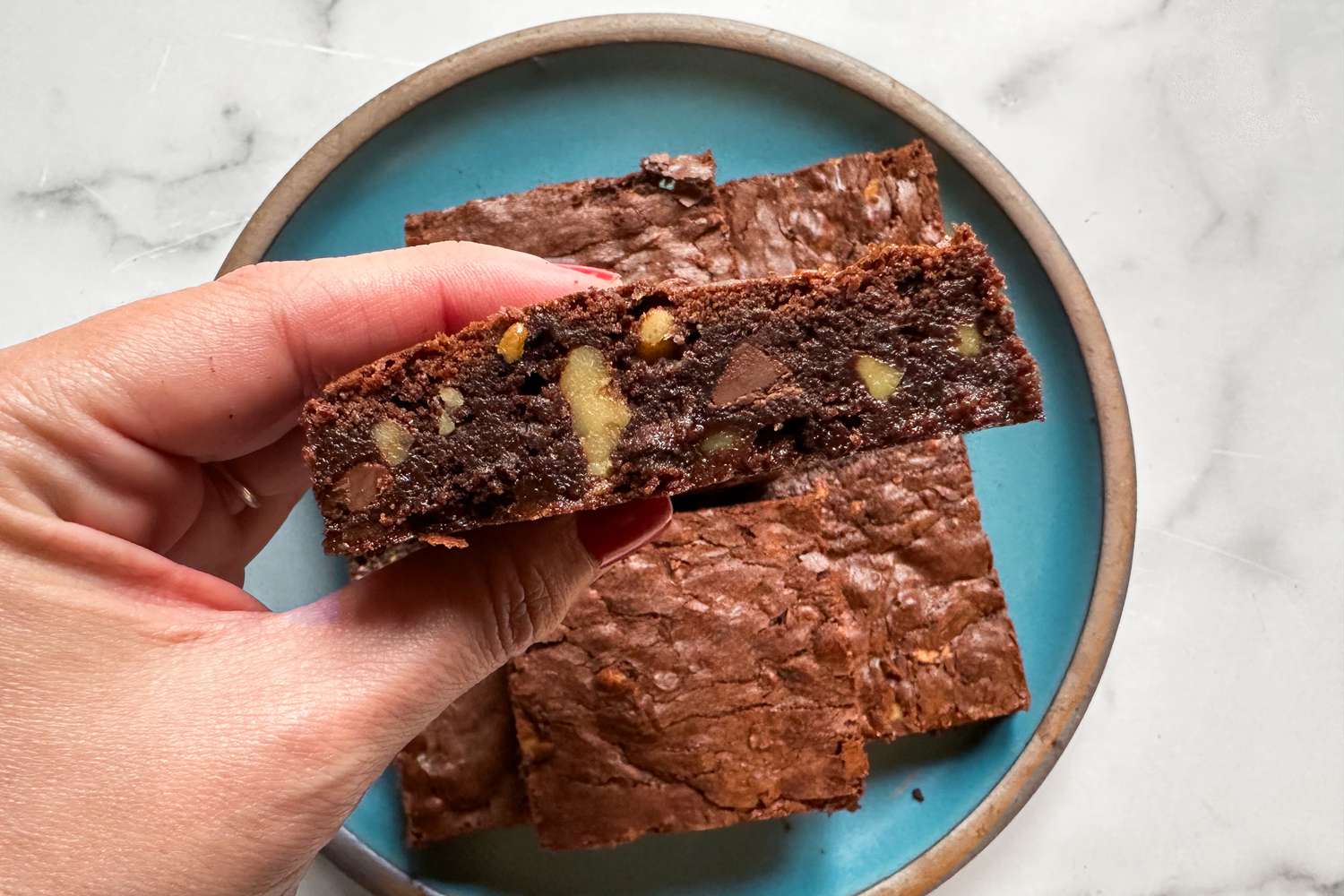 Closeup of a hand holding a brownie, showing its fudgy center