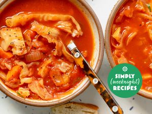 Two bowls of soup with a tomato base and pasta accompanied by bread