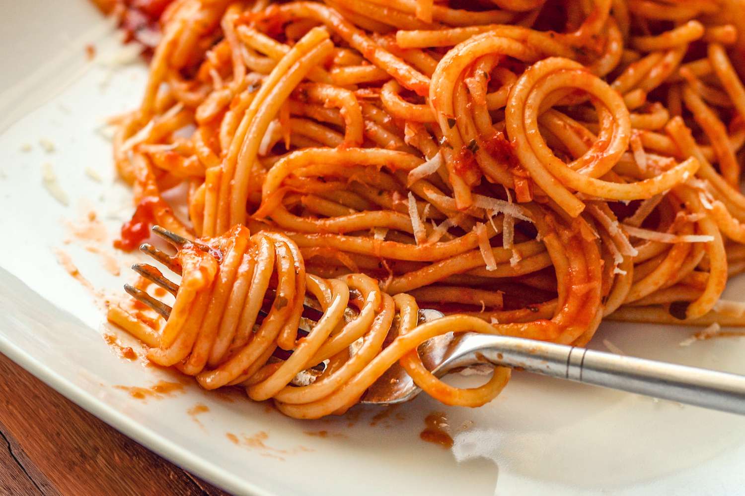 pasta (in marinara sauce) wrapped around a fork on a plate with more sauced pasta