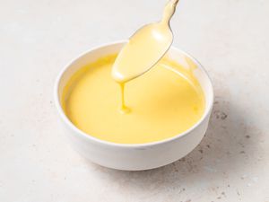 Blender Hollandaise Sauce in a white bowl with sauce dripping off of a spoon.