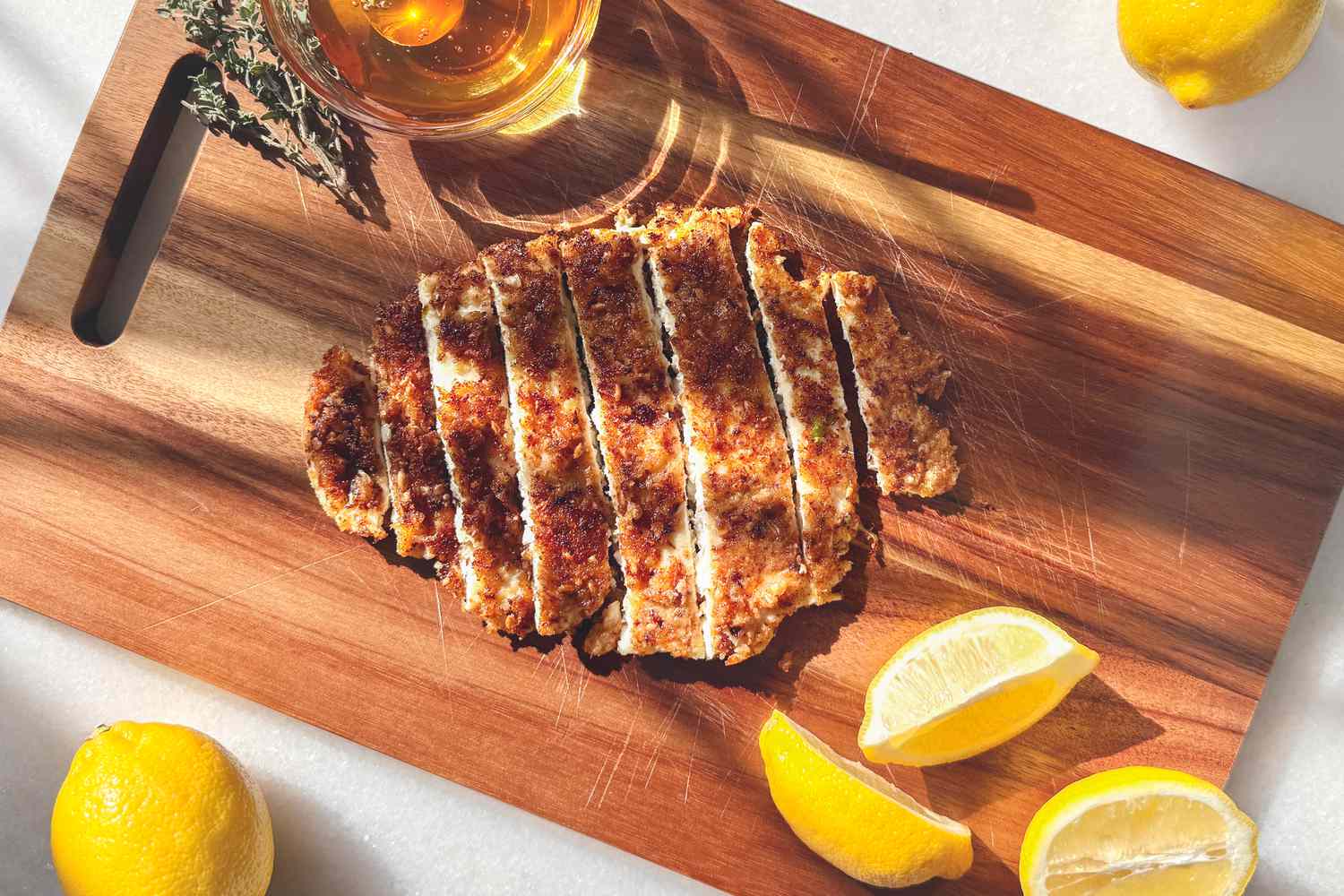 Overhead shot of a sliced cooked chicken breast on a wooden cutting board with lemon wedges