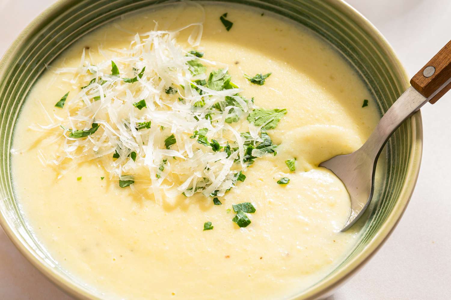 A bowl of creamy potato soup topped with shredded cheese and chopped herbs served with a spoon