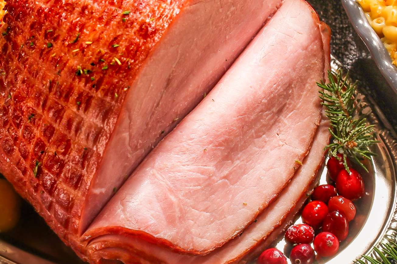Sliced cooked ham served on a platter with garnishes like cranberries and herbs