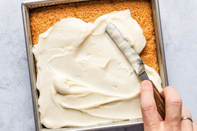 A hand spreading frosting over a square cake using an offset spatula
