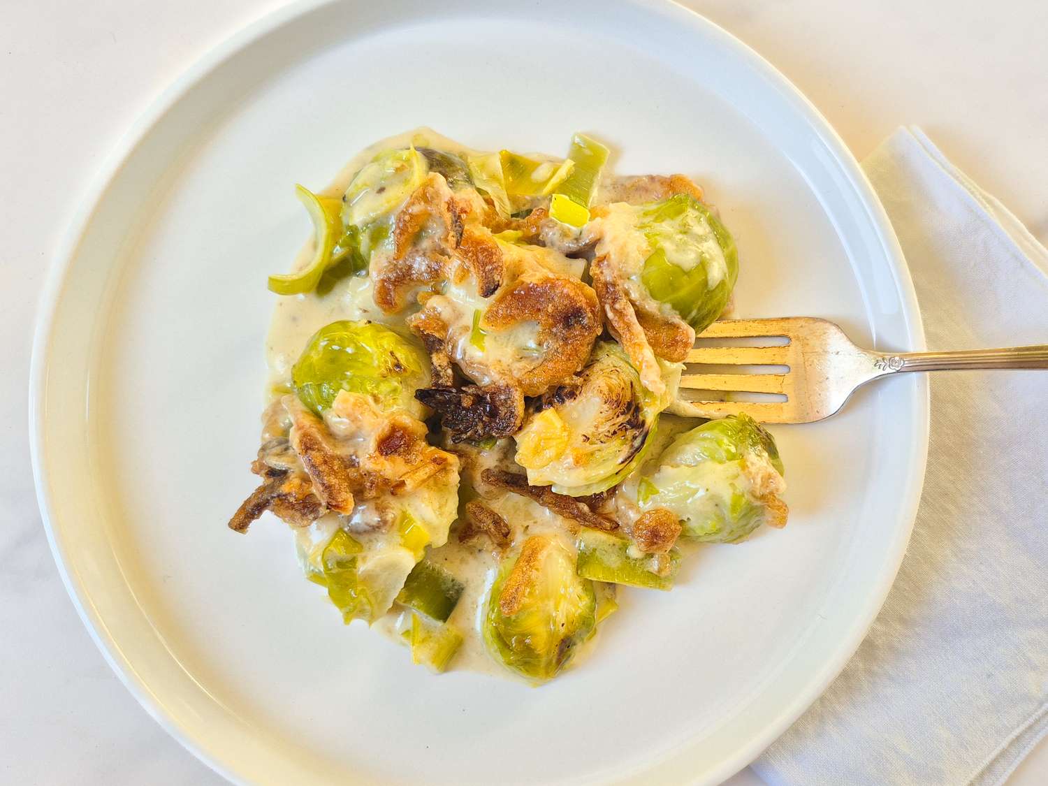 A plate with cooked Brussels sprouts in a creamy sauce with a fork on the side