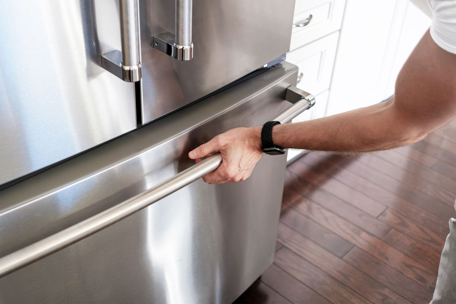 Person opening the bottom freezer of a stainless steel refrigerator in a kitchen