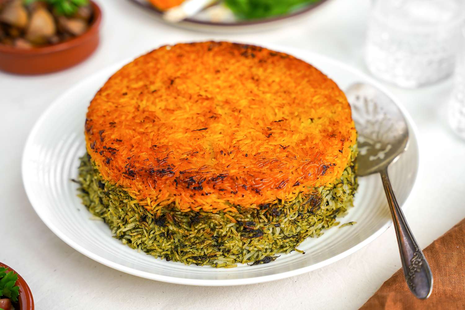 Sabzi Polo (Persian Herb Rice) on a Plate at a Table Setting With Sides (in the Background) and Glasses of Water 