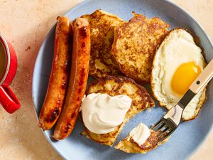 Overhead view of Irish boxty with a side of eggs and sausage next to a fork with a bite on it on a plate, all next to a coffee mug on a stone countertop