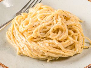 A plate of spaghetti with cream sauce and black pepper fork on the side