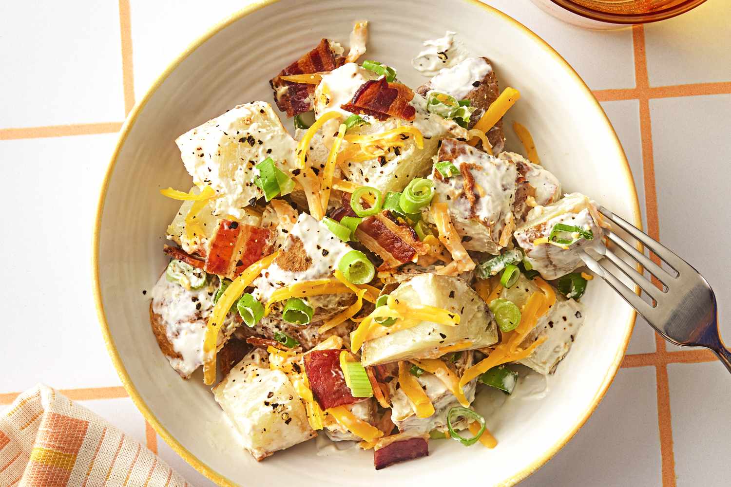 A dish of loaded potato salad with chopped green onions shredded cheese and bacon served in a white bowl