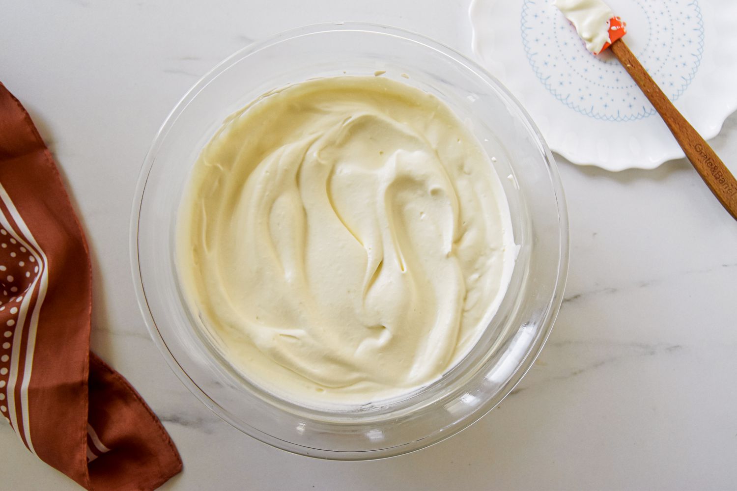 Bowl of whip cream next to a brown kitchen linen and a small plate with a spatula for easy pumpkin mousse recipe