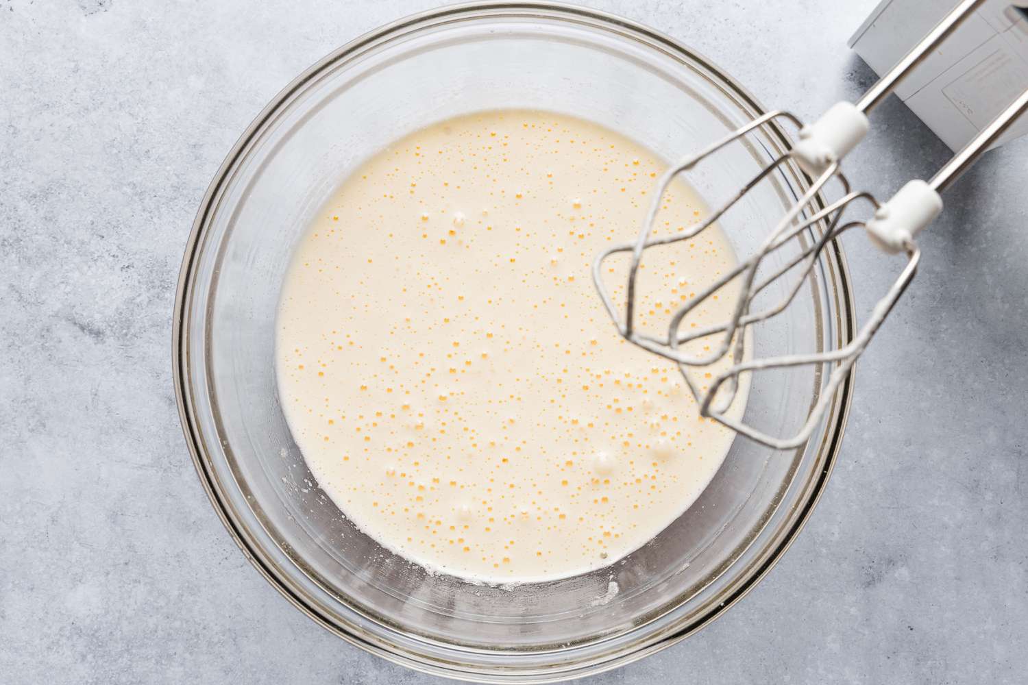 bowl with mixed wet ingredients, hand mixer beaters coated with wet ingredients positioned over the top of the bowl - Feather Cake