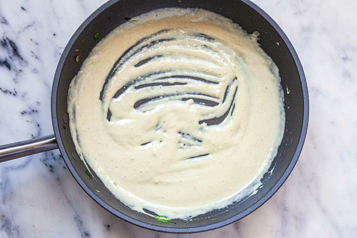 A non-stick skillet with a cream sauce at the bottom to show how to make creamed spinach.