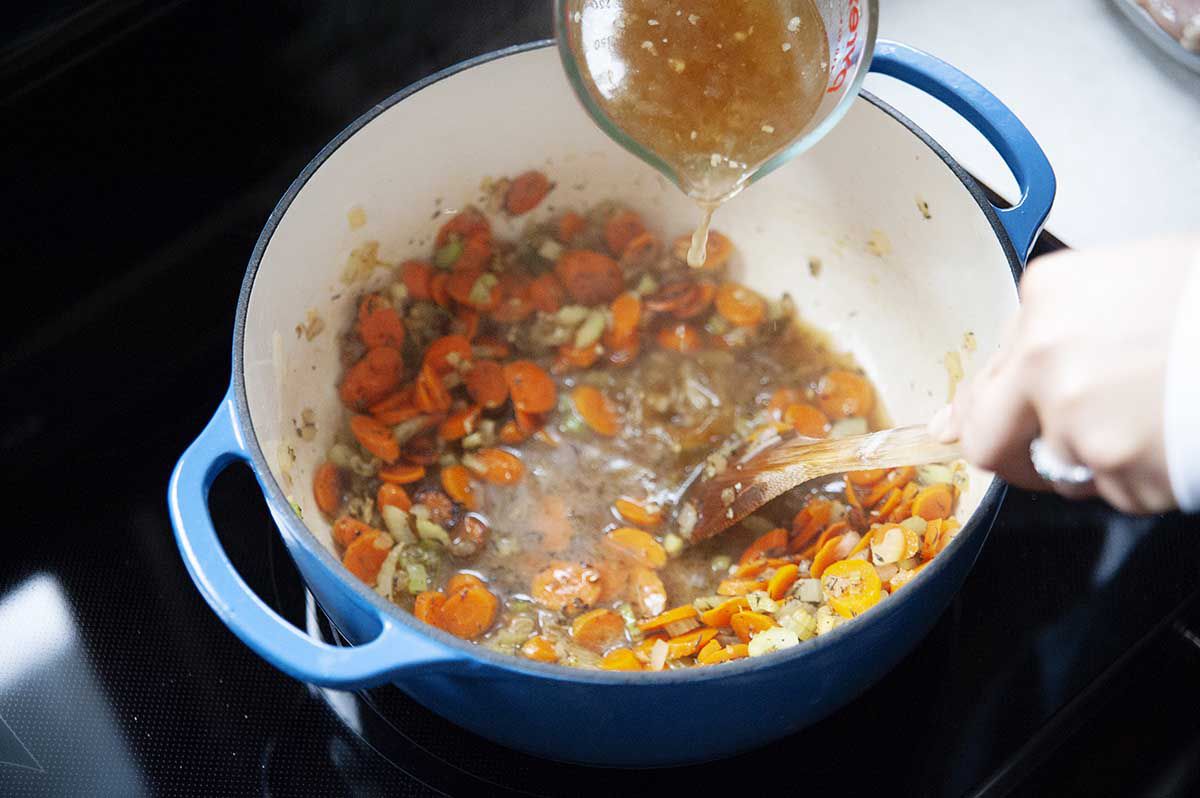 Stock being used to delgaze the bottom of the pan filled with vegetables.
