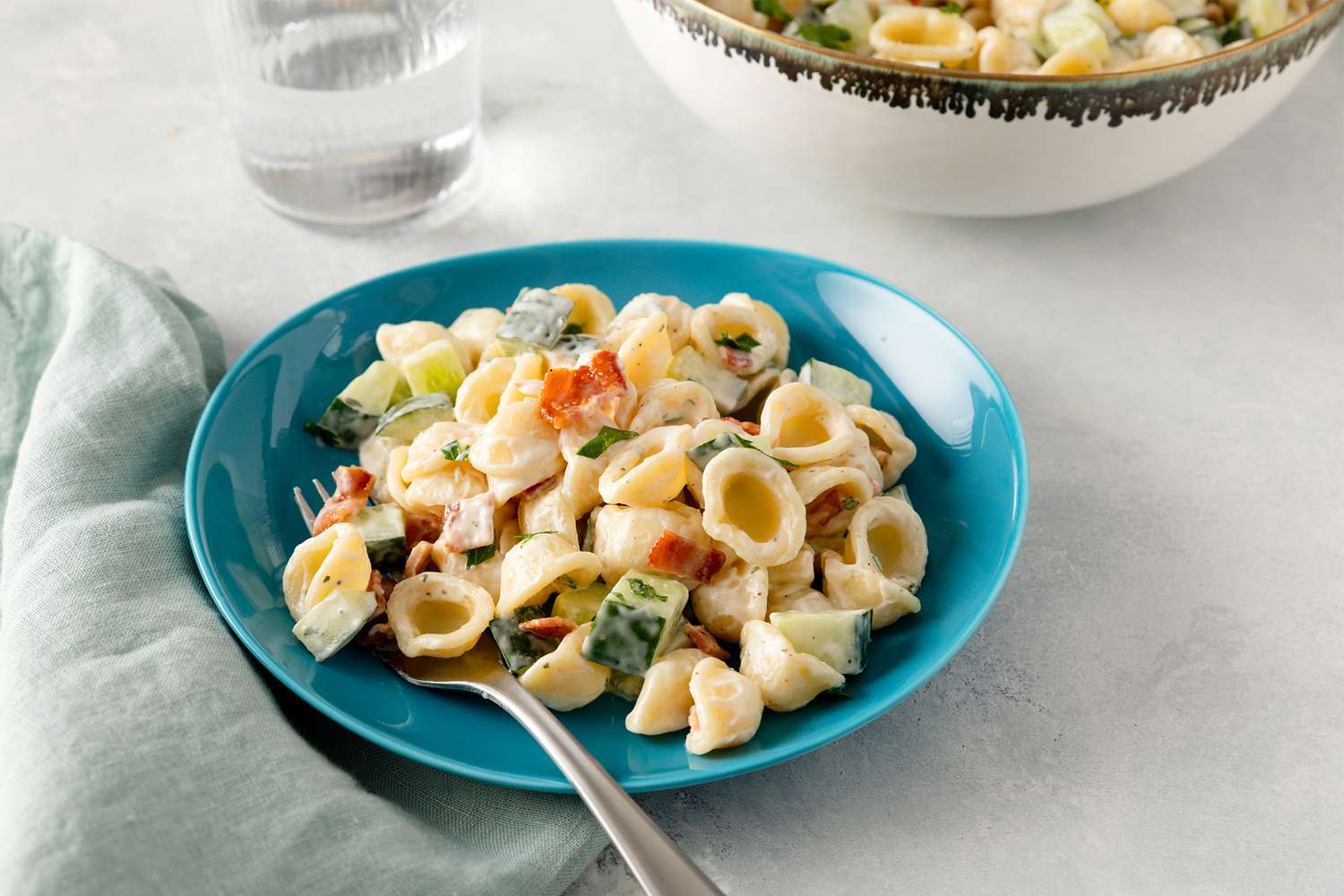 Pasta salad with shell pasta diced cucumbers bacon and creamy ranch dressing served on a blue plate