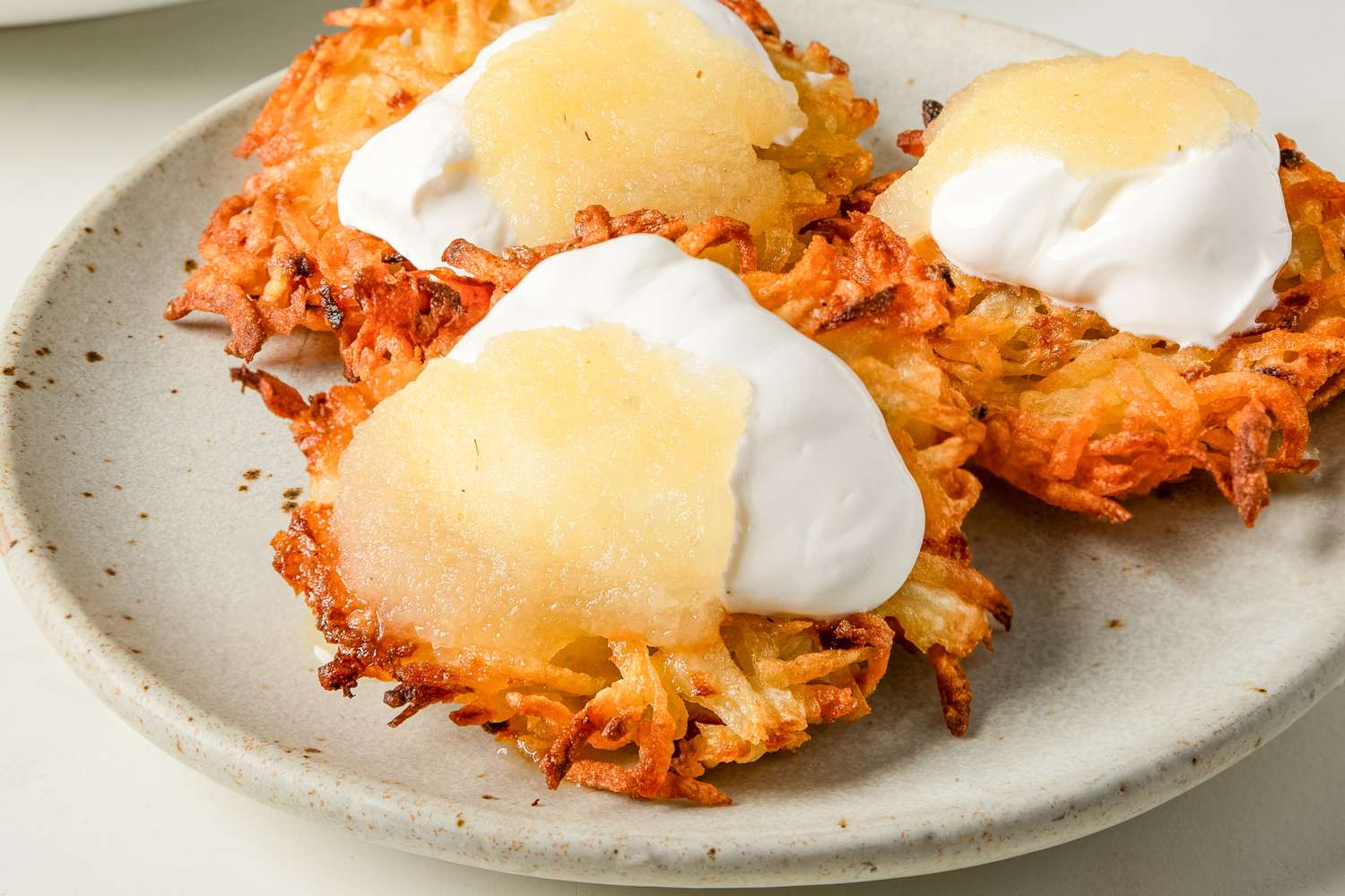 Latkes topped with applesauce and sour cream on a plate