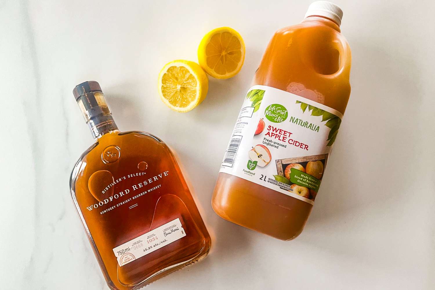 Bottle of whiskey bottle of apple cider lemon halves displayed on a surface