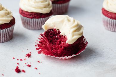 A red velvet cupcake set in a cupcake liner with a bite taken out of it.