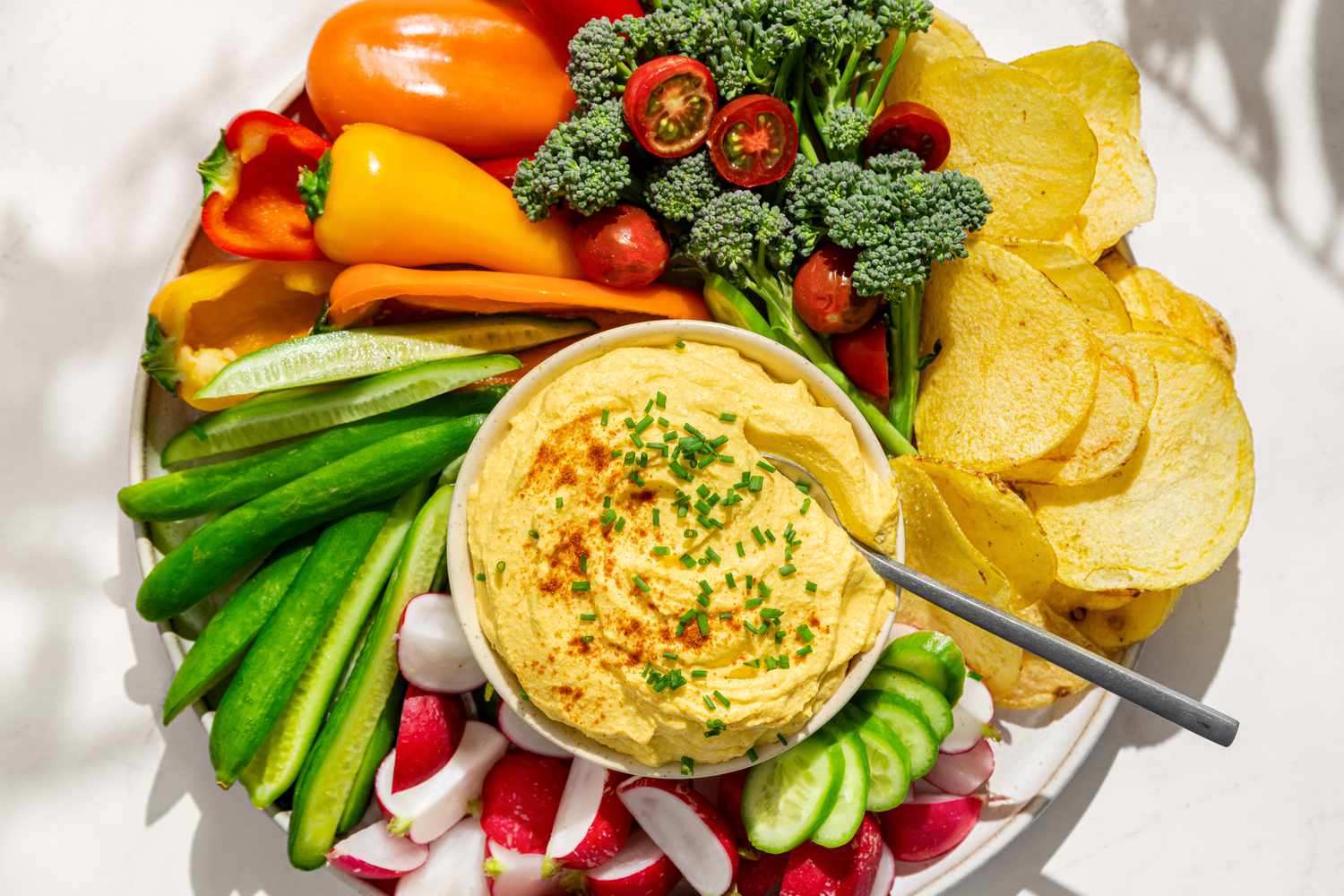 Overhead view of a platter with vegetables and potato chips arranged around a bowl of deviled egg dip all on a white background