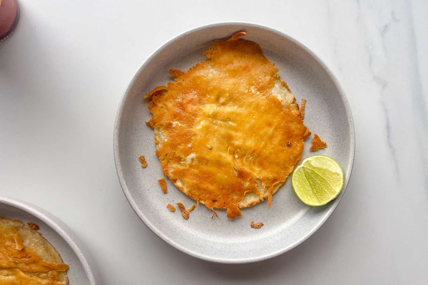 A plate with a crisped tortilla covered in melted cheese accompanied by a lime wedge