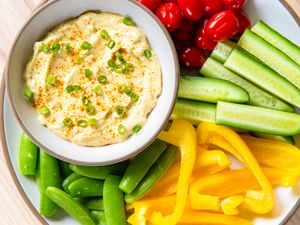 Bowl of curry dip surrounded by fresh vegetables including cucumbers, yellow peppers, snap peas, and tomatoes