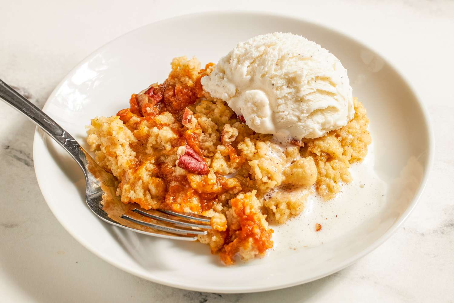 A serving of dessert on a plate featuring pumpkin dump cake with ice cream