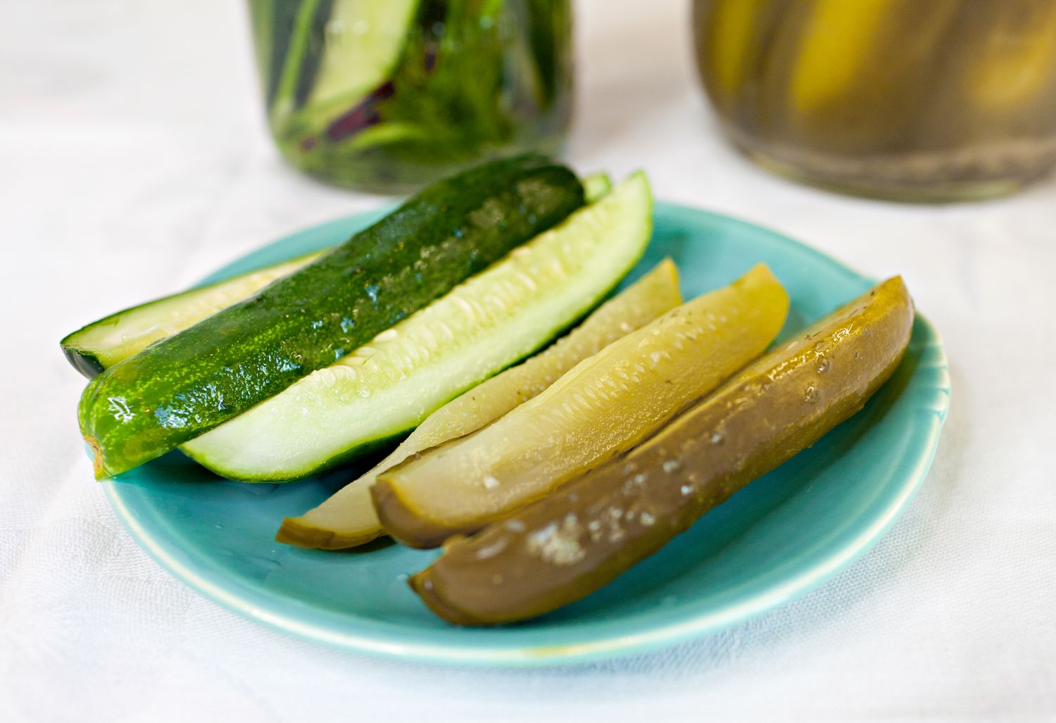 Fermented Pickles on a Small Plate with More in Jars in the Background
