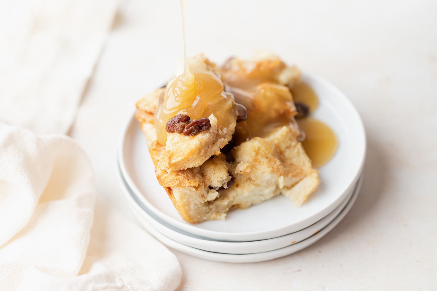 Bread pudding with bread pudding sauce on a stack of plates.