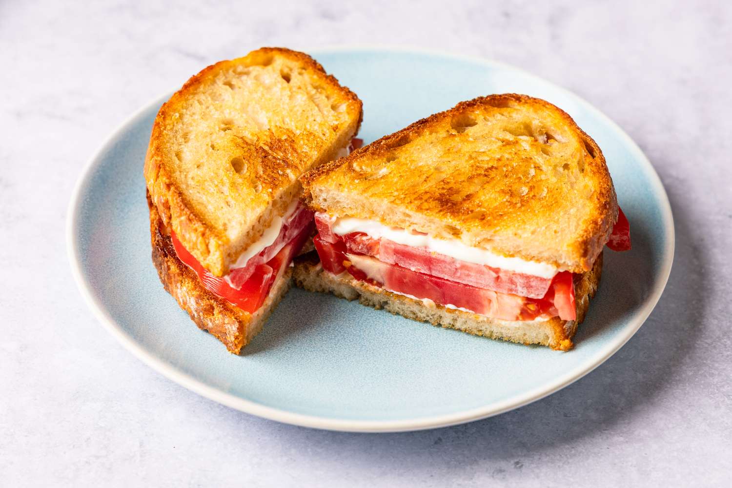 A sandwich with tomato slices and a creamy filling on toasted bread cut in half and served on a plate