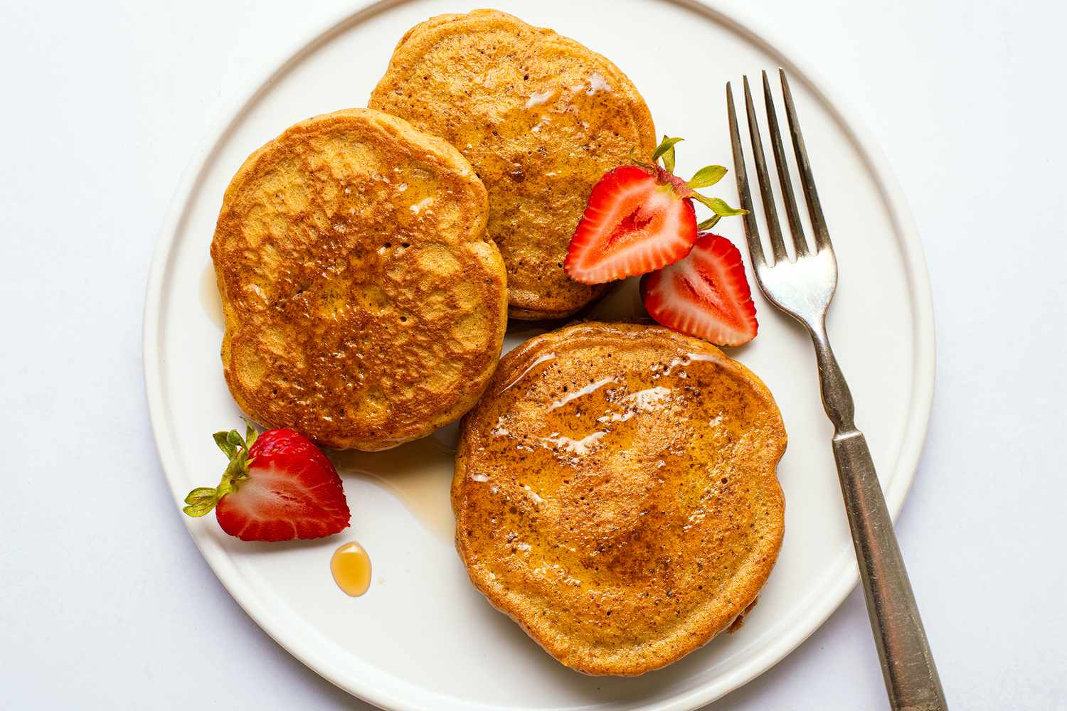 Plate with three almond butter pancakes garnished with strawberries and syrup