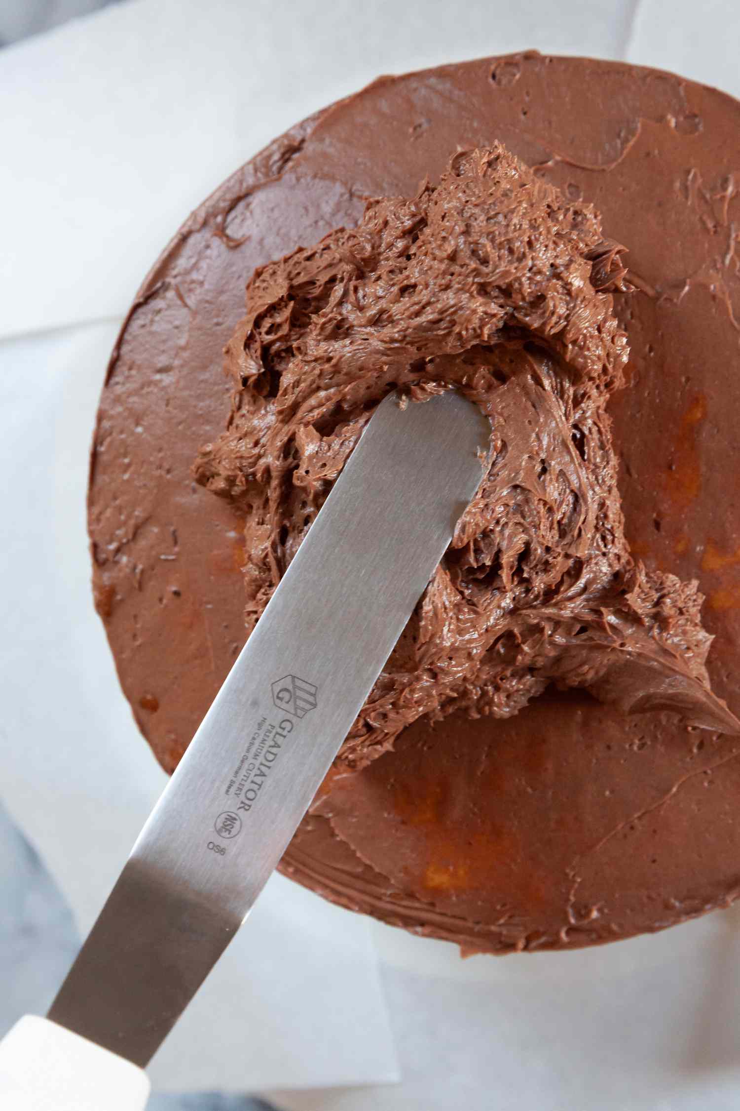Overhead view showing how to frost a layer cake with chocolate frosting.