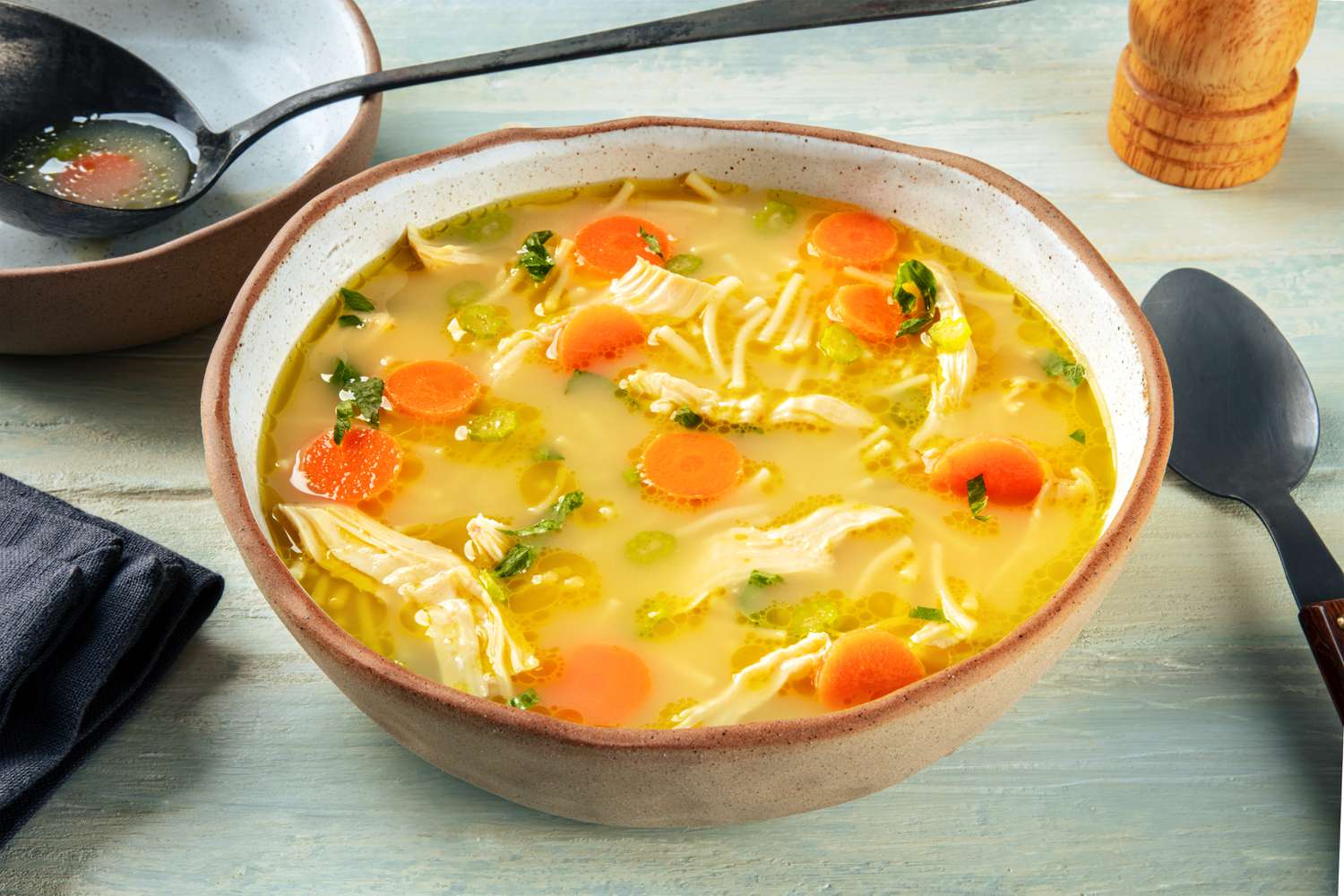 A bowl of chicken noodle soup with carrot coins, shredded chicken, and short noodles
